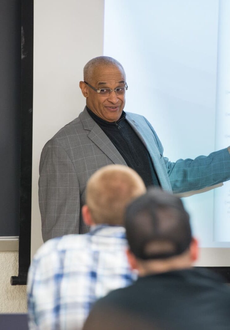 Prince Wells teaching class 01-18-17 diverse faculty A man standing in front of a projector screen.